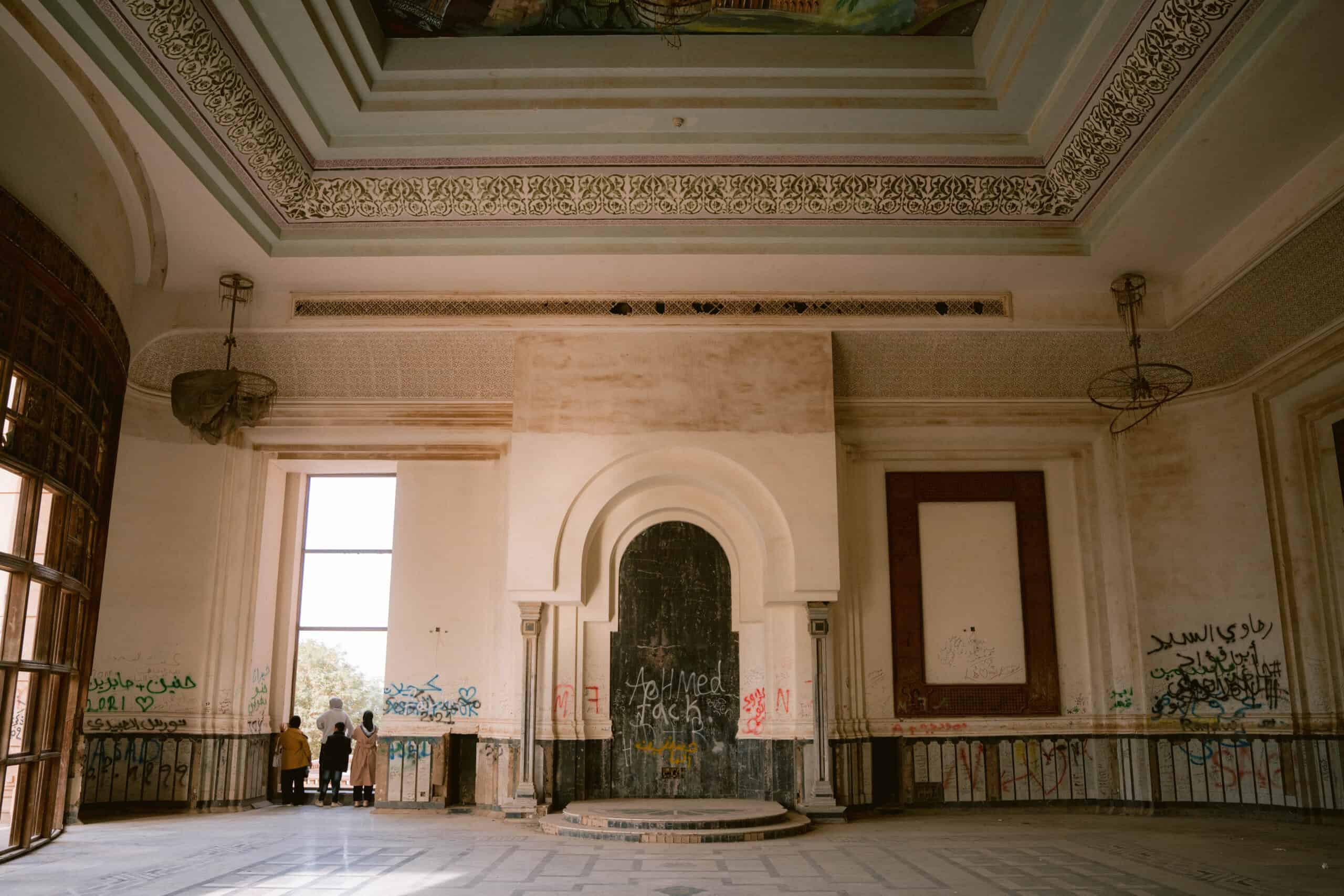 Interior of Saddam Hussein’s abandoned palace near Babylon, showing ornate arches, faded walls, and graffiti covering the former throne area.
