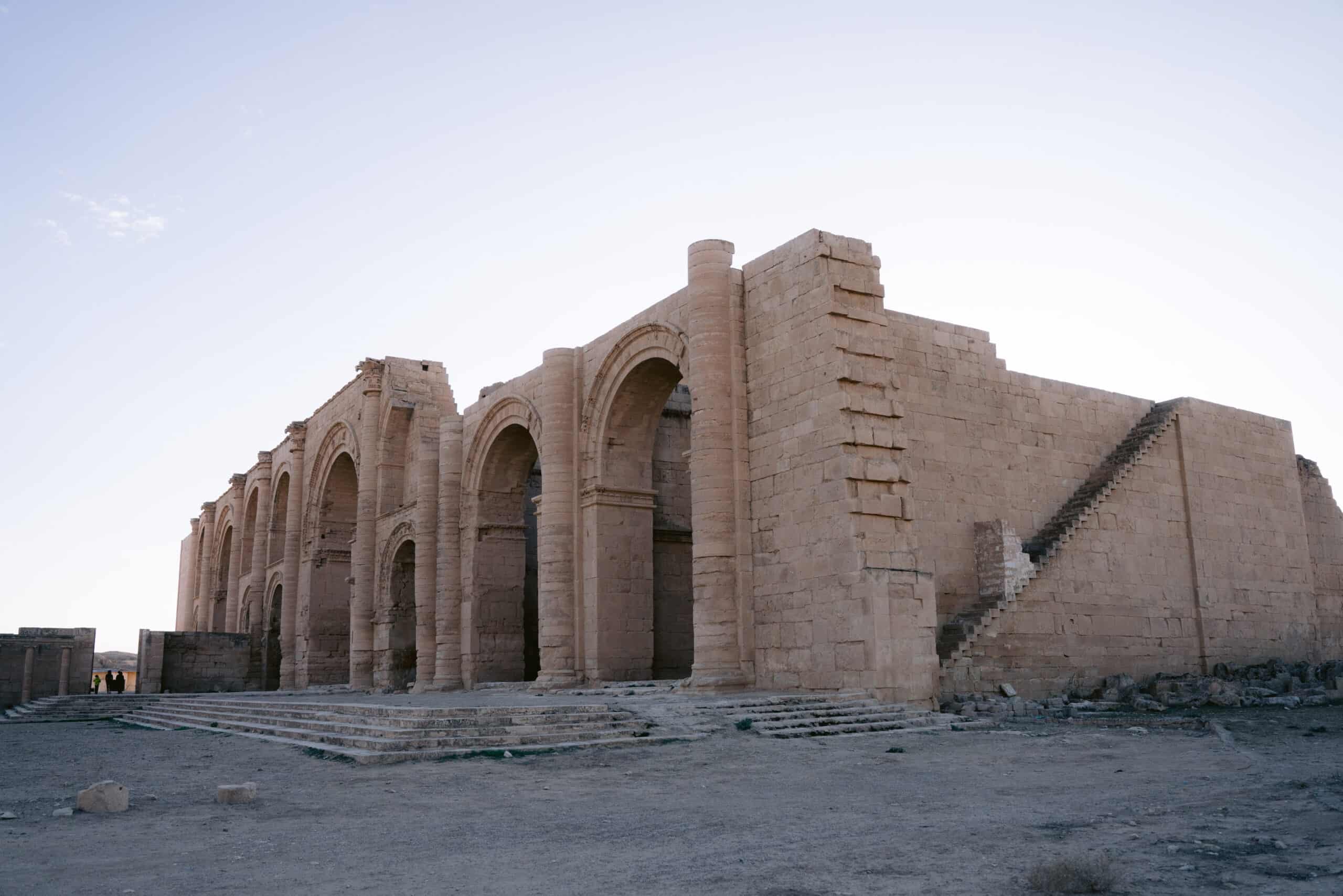 Stone arches and staircases form the remains of a temple complex at Hatra, casting long shadows in the late afternoon light.