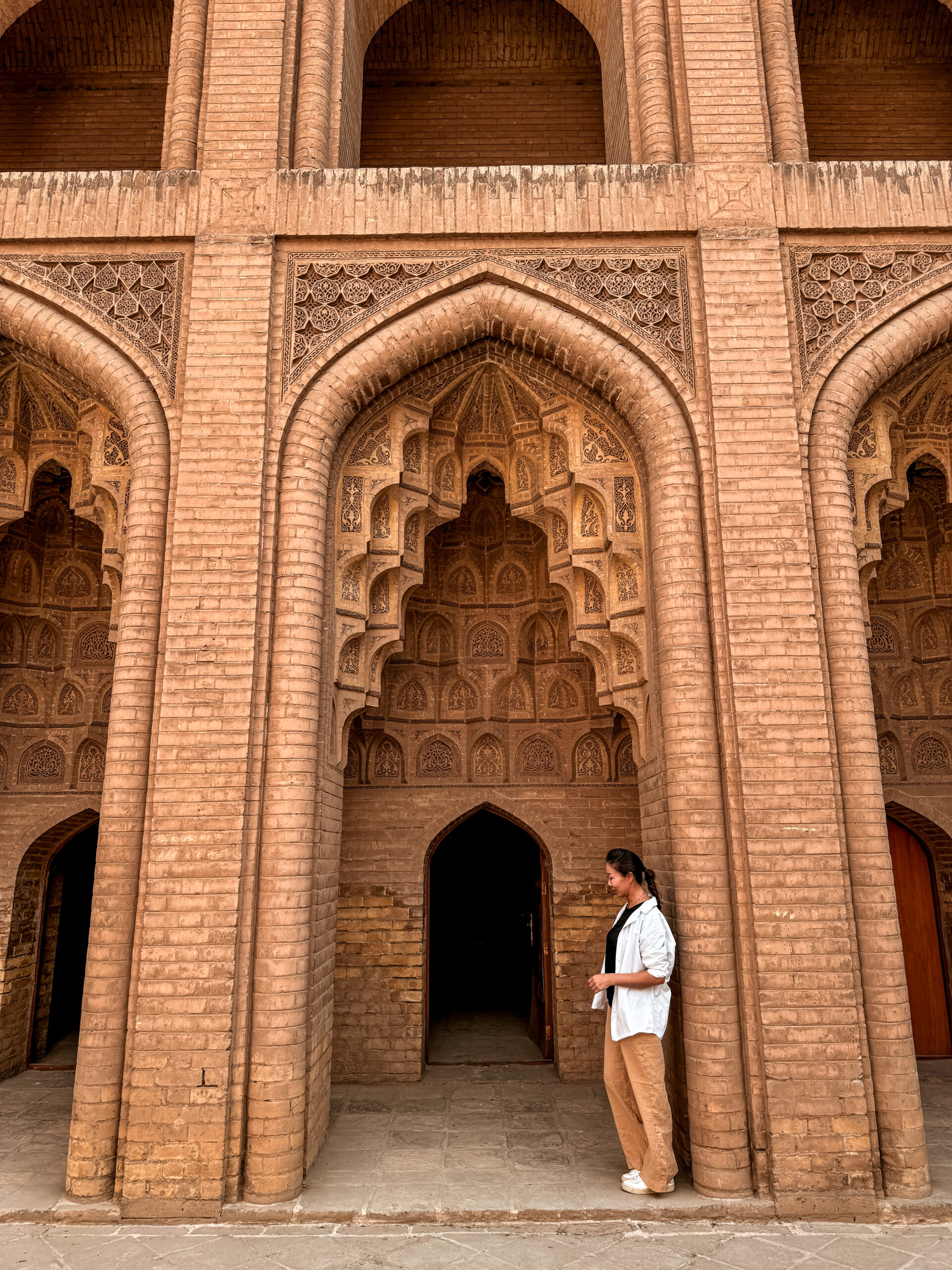Traveler standing beside an arched doorway at Abbasid Palace in Baghdad, Iraq, showcasing the detailed brick architecture of one of the last remaining structures from the Abbasid era—one of the top places to visit in Baghdad for history lovers.