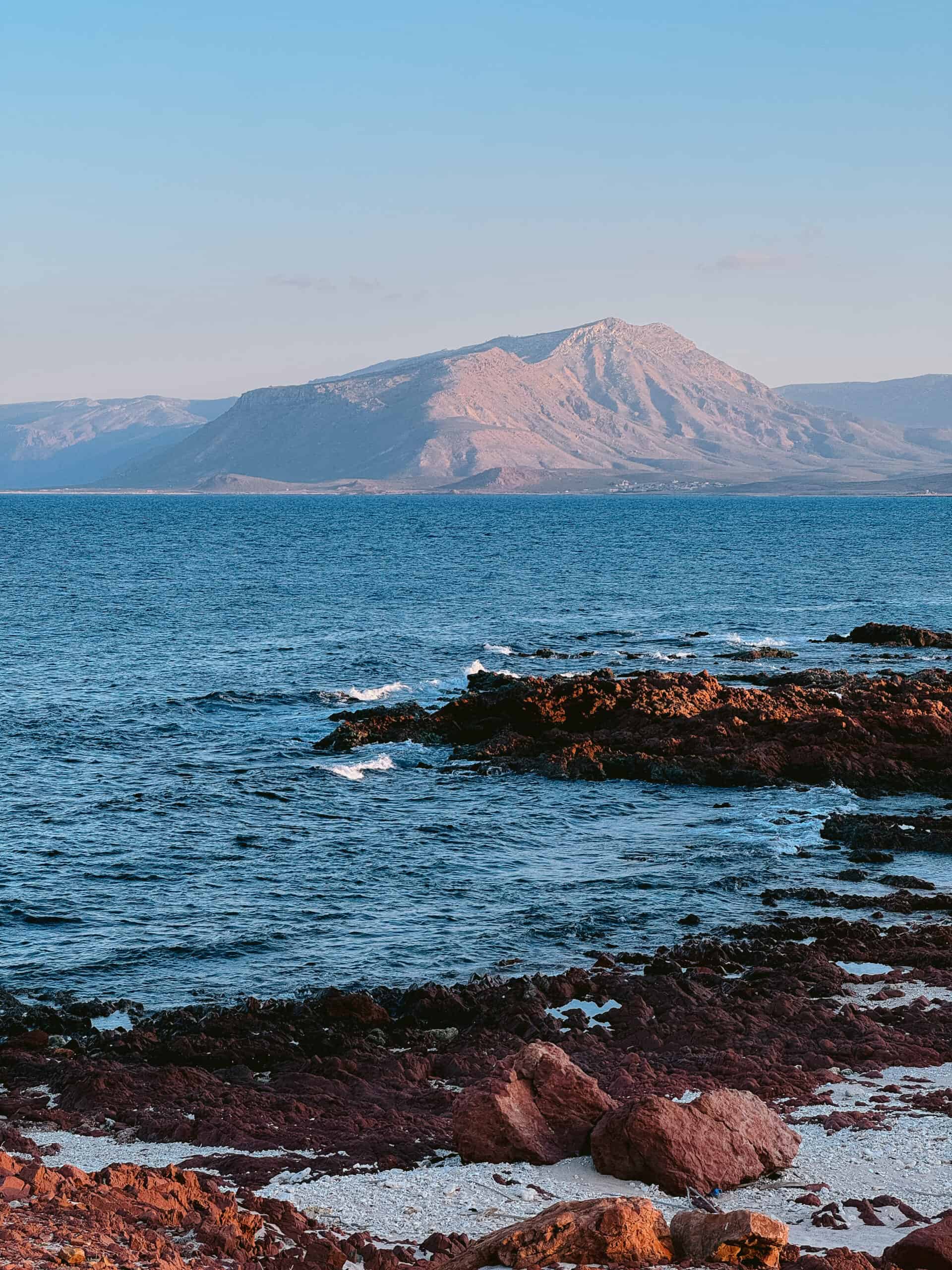 Rocky shoreline with volcanic red rocks and turquoise waters at a top snorkeling beach on Socotra Island, Yemen — a must-visit stop for marine life and adventure seekers exploring things to do in Socotra.