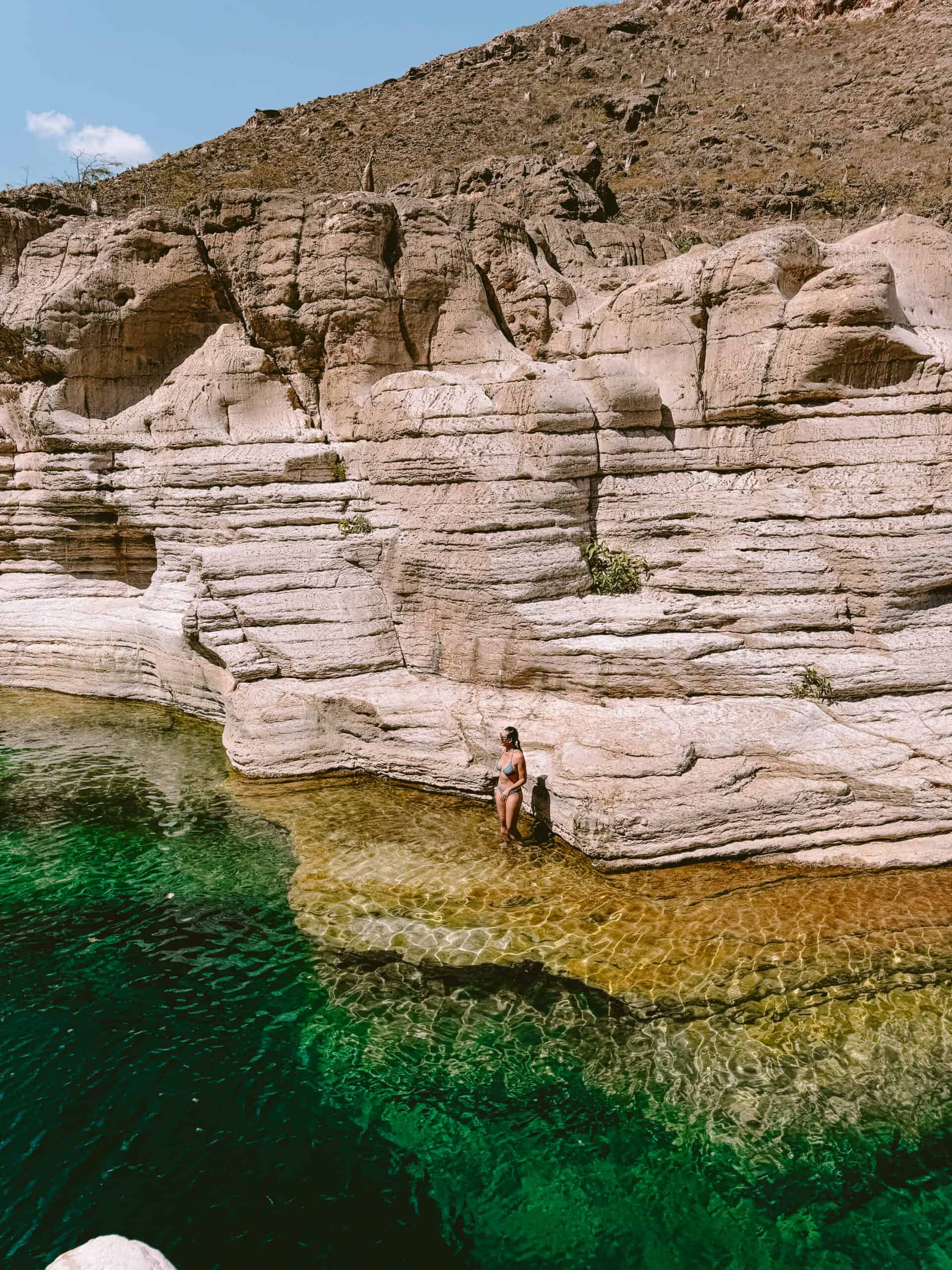 Traveler standing in the shallow emerald waters of Wadi Kalisan, Socotra, surrounded by dramatic layered rock cliffs — a hidden gem for safe, offbeat adventures in Yemen.