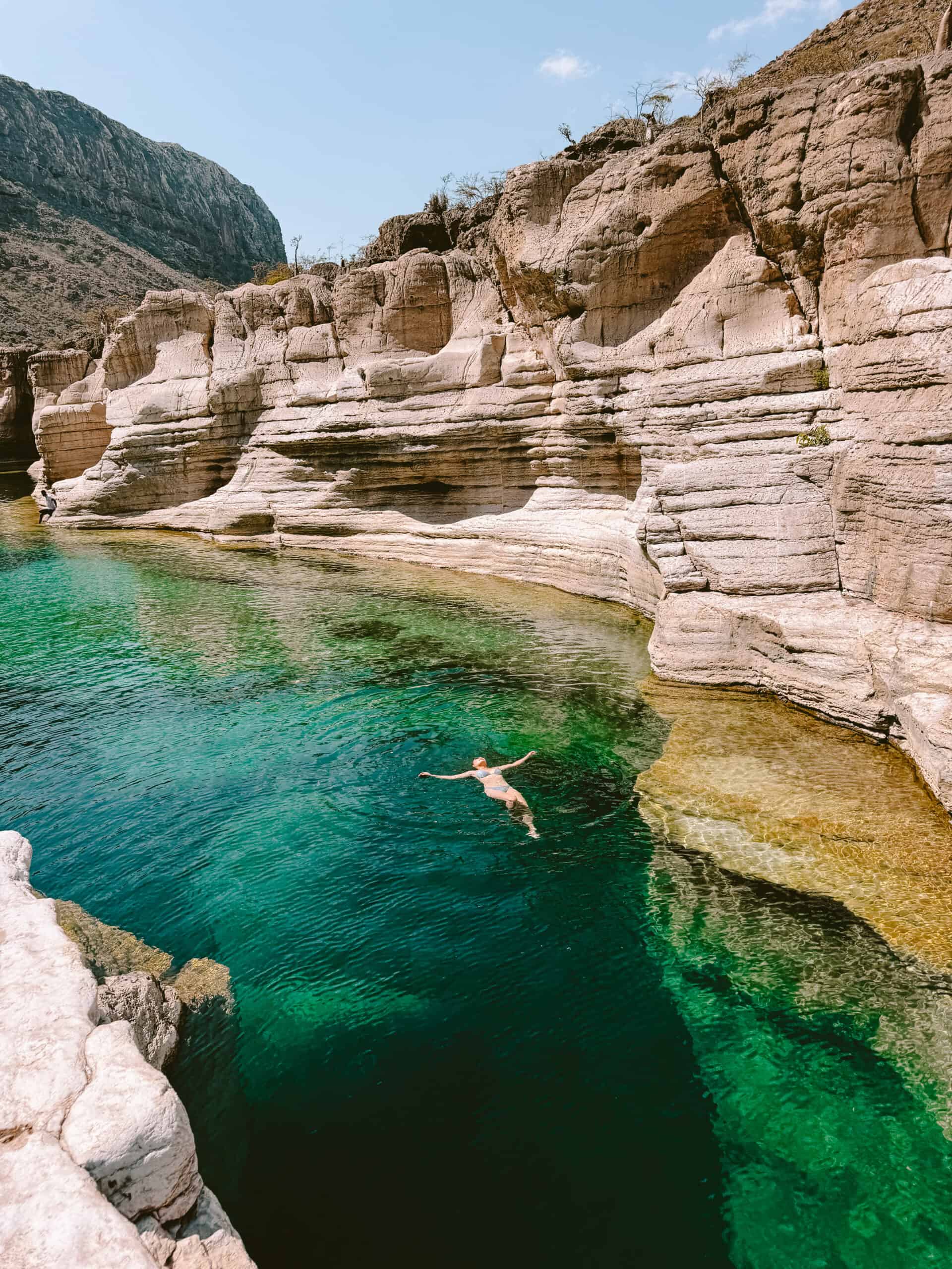 Woman floating in the deep turquoise waters of Wadi Kalisan, Socotra, framed by towering limestone cliffs — a serene and safe swimming spot in Yemen’s remote island paradise.