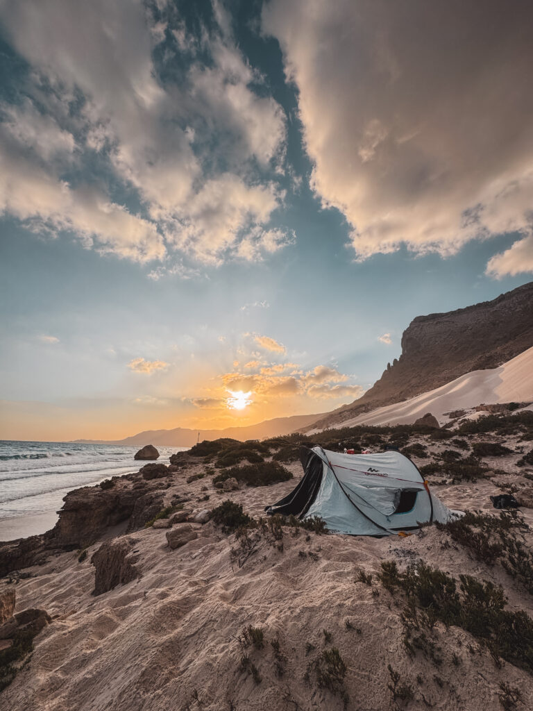 Tent camping on Socotra’s beach at sunset with sand dunes, rocky cliffs, and the Arabian Sea, showing a peaceful and safe side of the island.