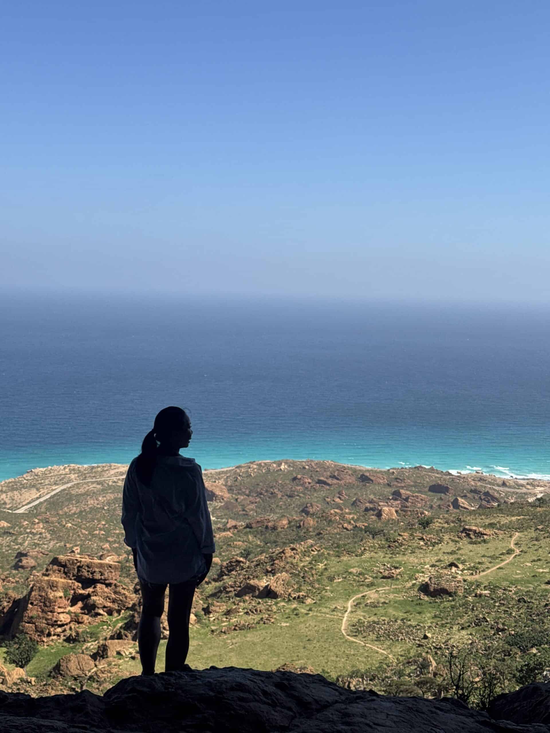 Silhouette of a woman standing inside Hoq Cave’s entrance, gazing out at the turquoise waters and rugged coastline of Socotra below, capturing one of the most breathtaking things to do in Socotra.
