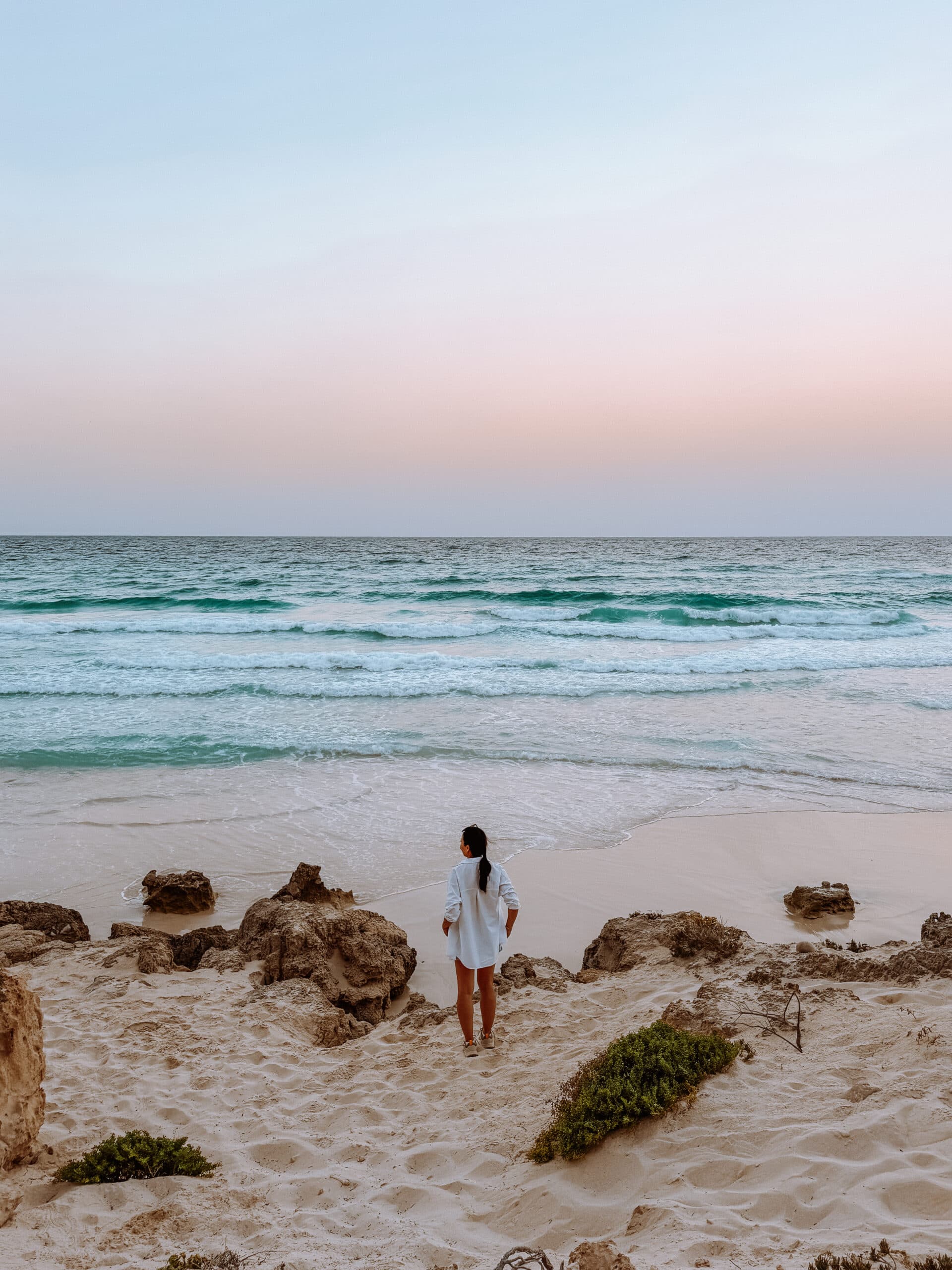 Traveler standing on a sandy beach at sunset in Socotra, Yemen, looking out at turquoise waves on the remote island.