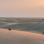 Footprints leading across the golden sand dunes of Socotra, Yemen, at sunset with the sea in the distance
