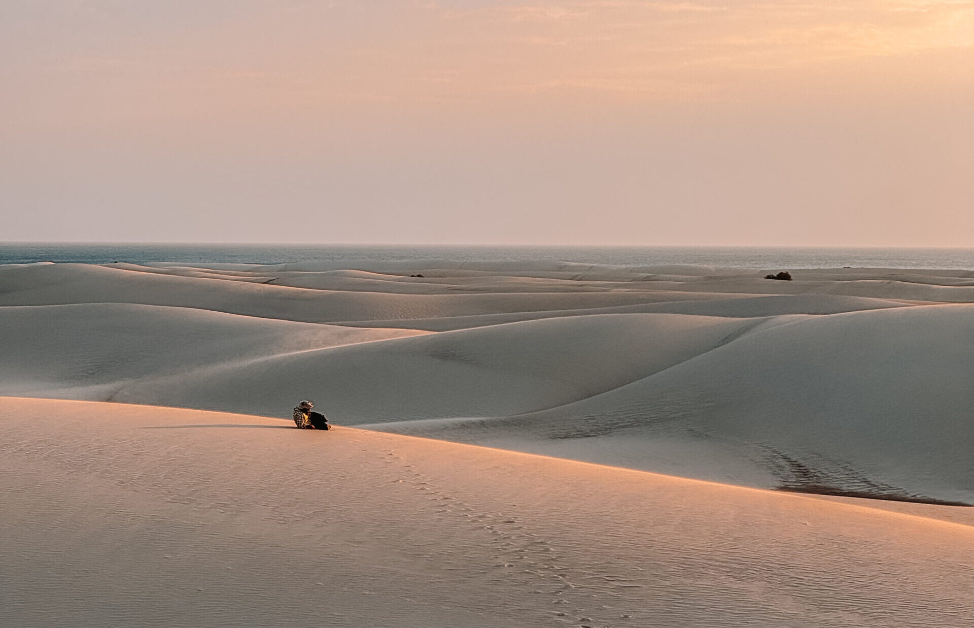 Footprints leading across the golden sand dunes of Socotra, Yemen, at sunset with the sea in the distance
