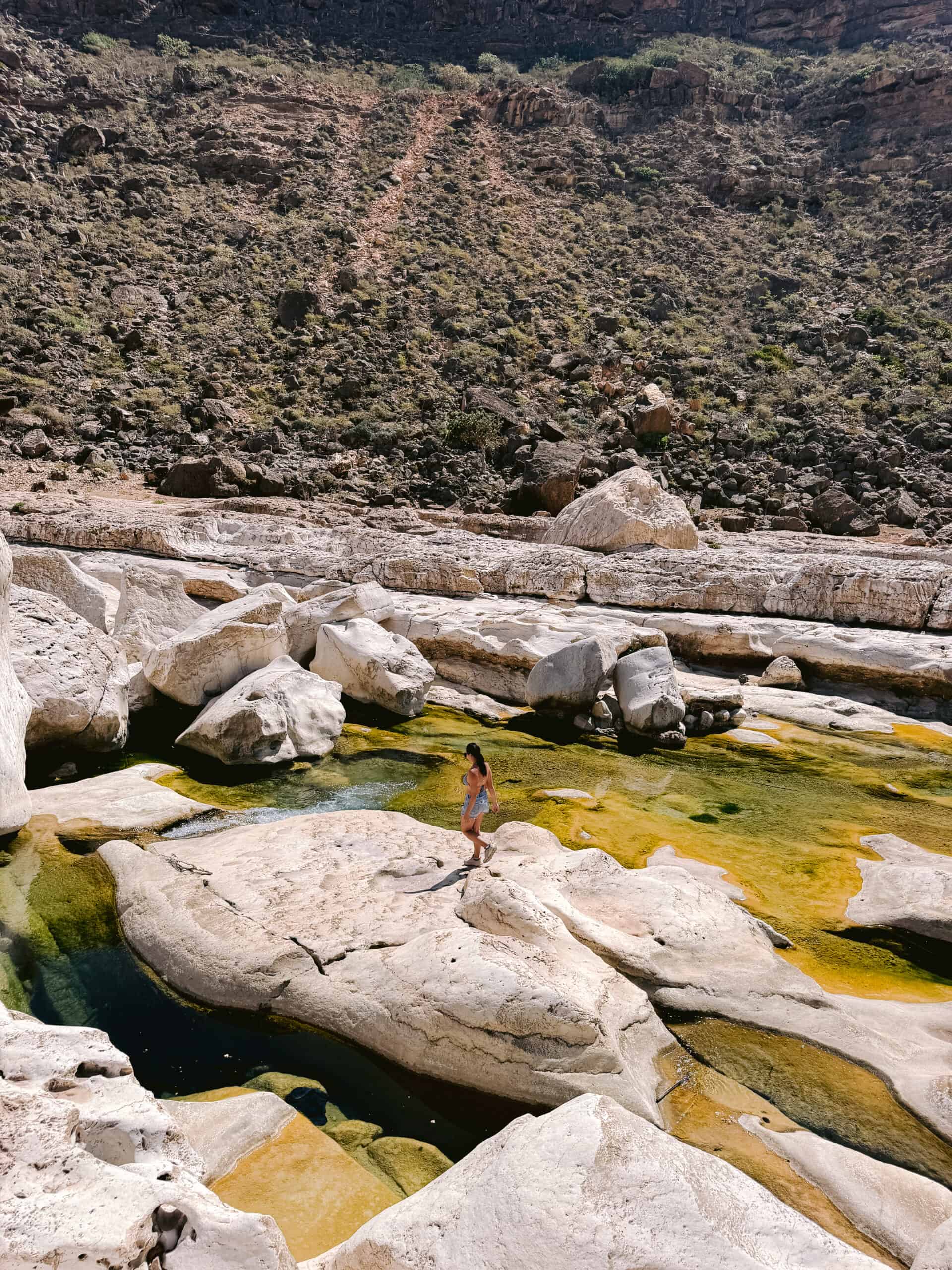 Traveler walking along rock pools in Wadi Dirhur canyon, Socotra Island.