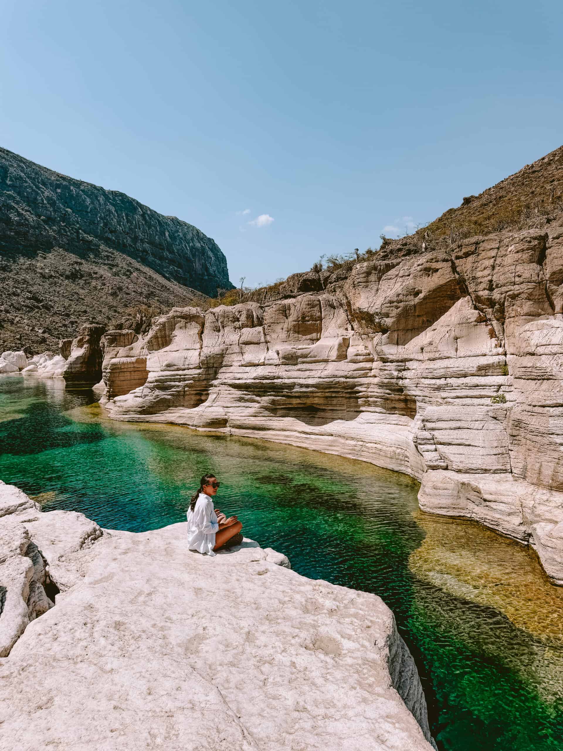 Traveler sitting by turquoise pools at Wadi Kalesan, Socotra Island.