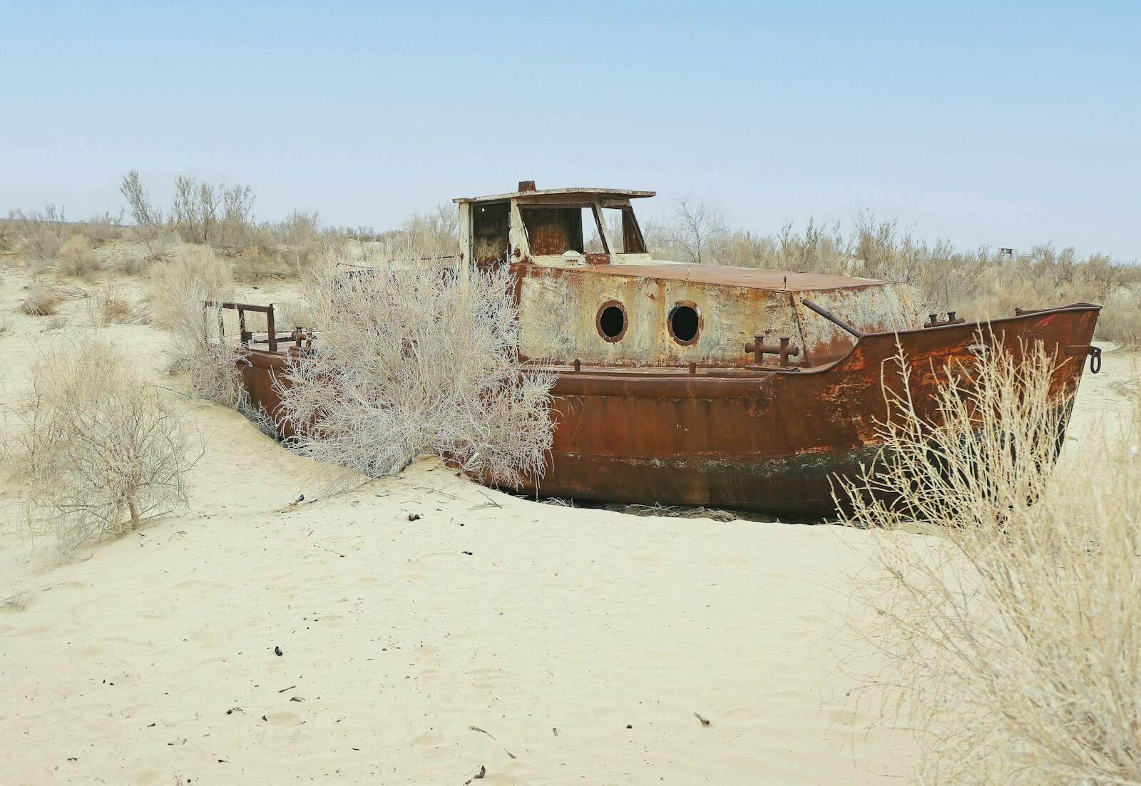 A rusty boat rests in the desert sand.