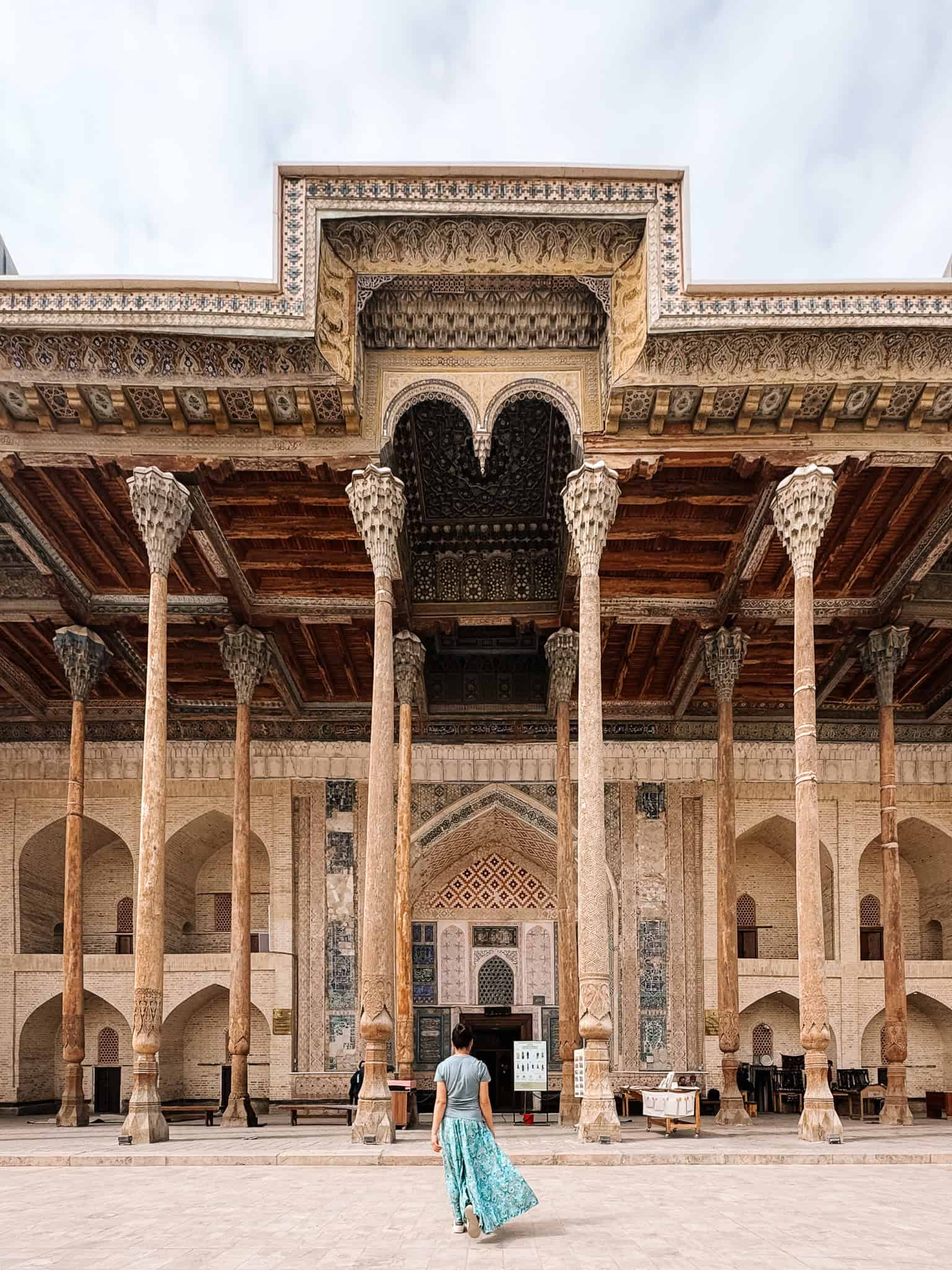 Solo female traveler walking toward a historic mosque in Bukhara, confidently exploring Uzbekistan and showing it is safe for women.