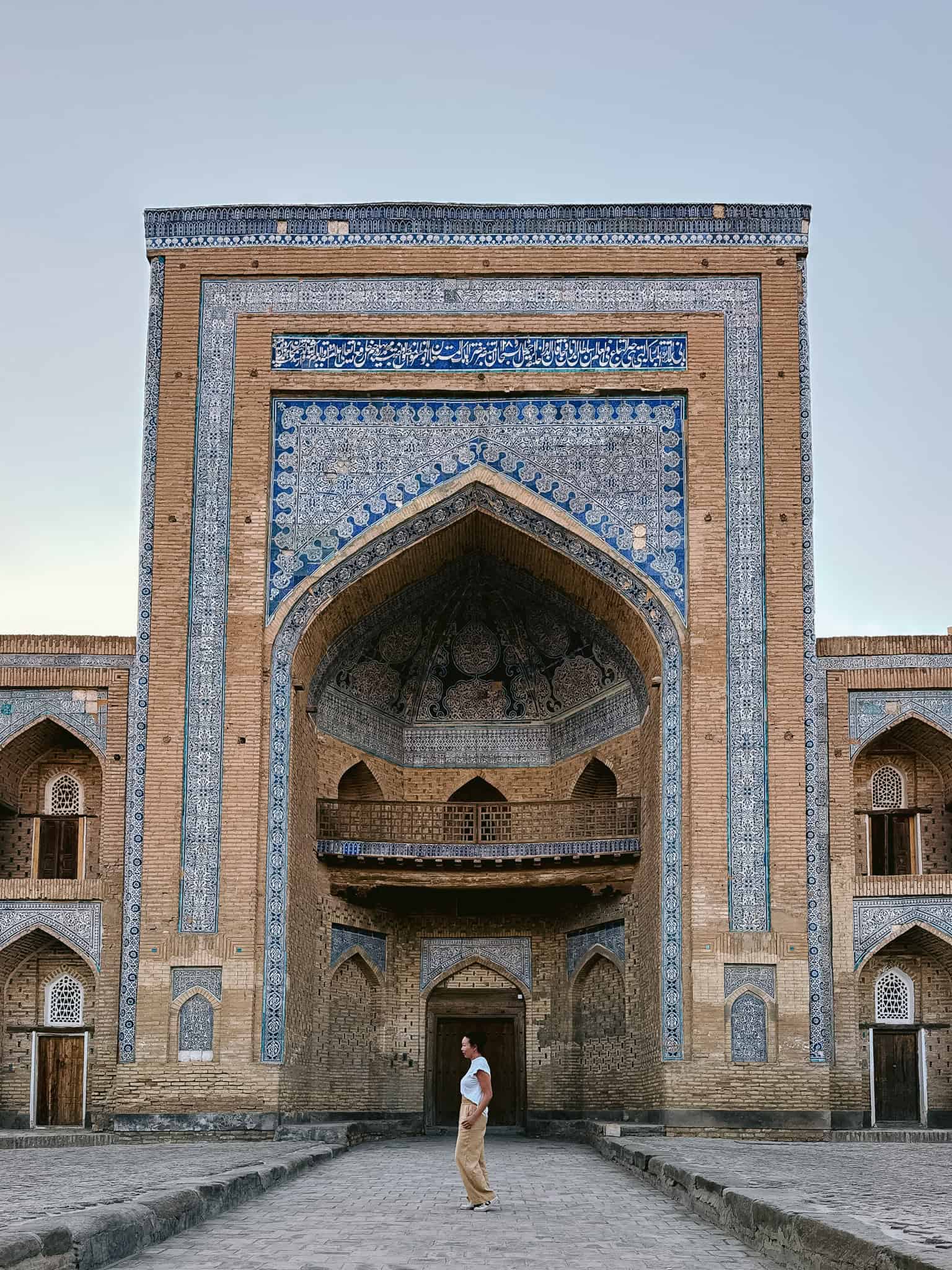 Modestly dressed woman walking near a blue-tiled madrasa in Khiva, showing respectful and safe solo travel in Uzbekistan.