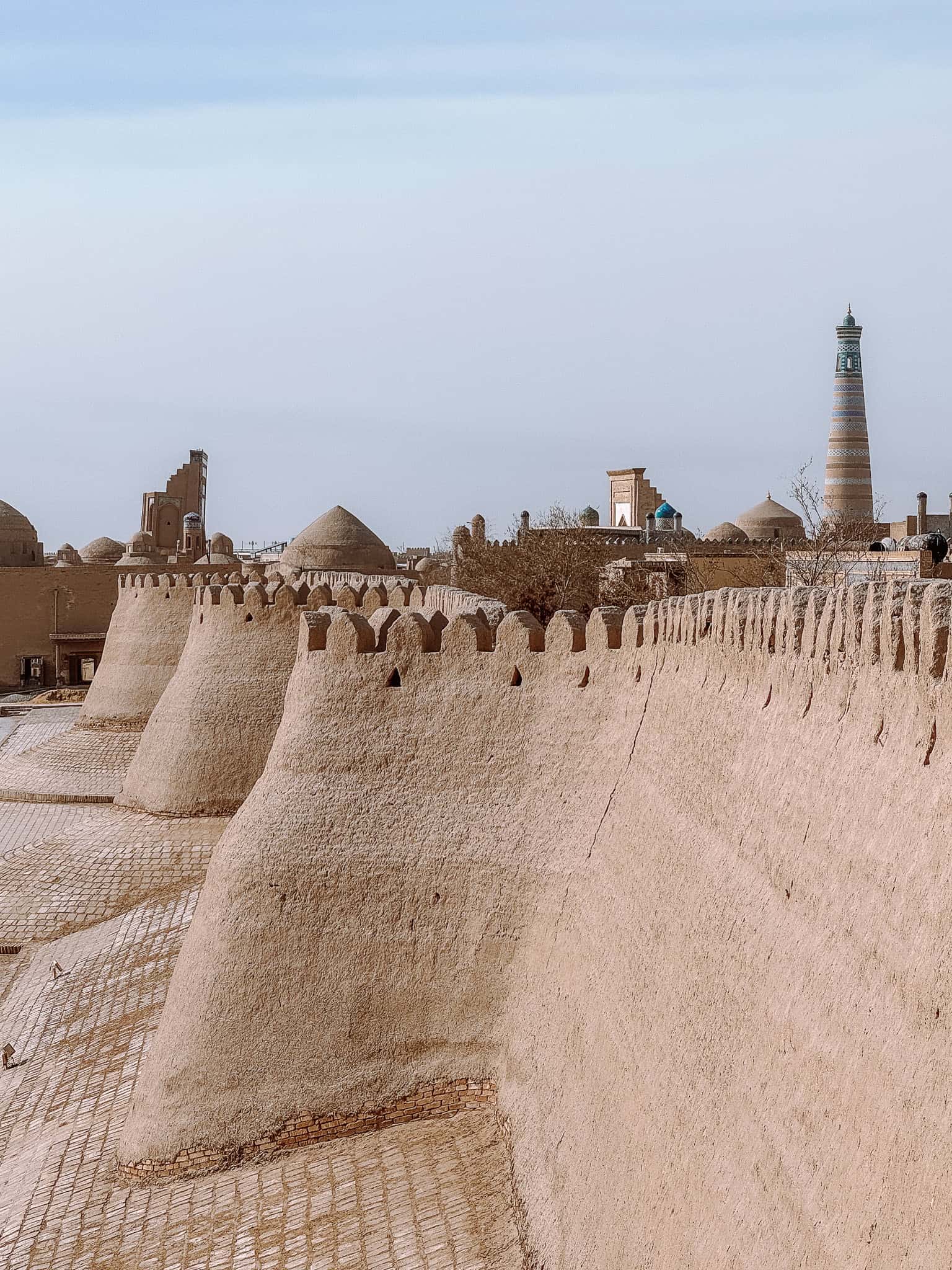View along the curved mudbrick city walls of Khiva’s Itchan Kala with minarets rising above the skyline.