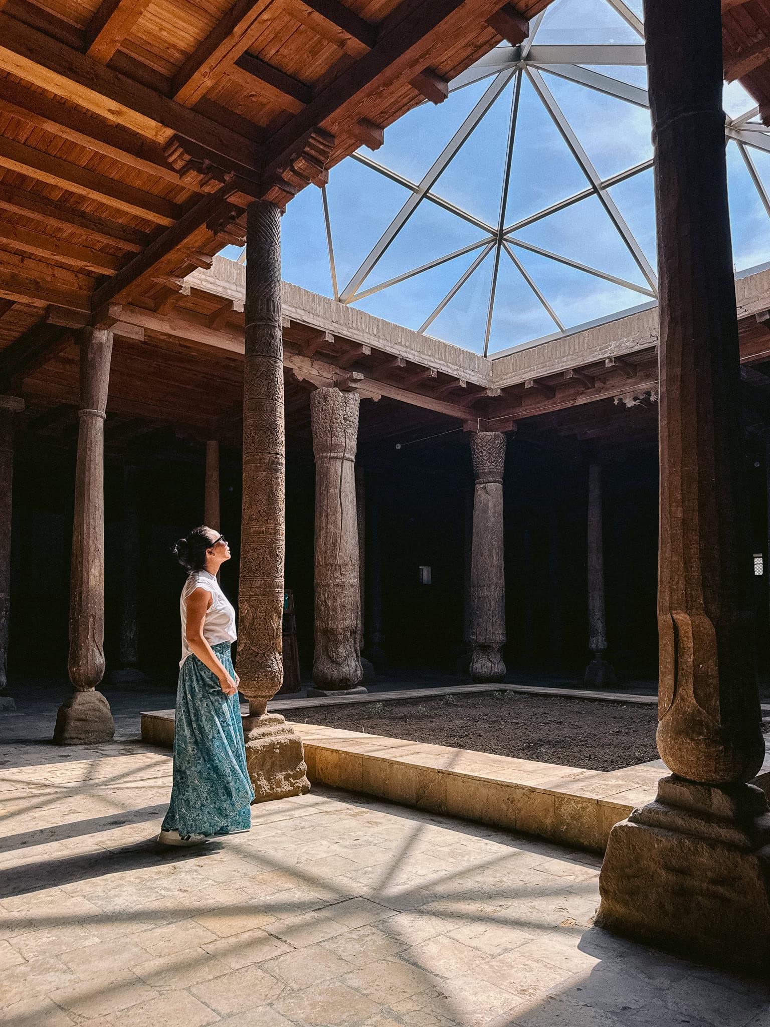 Traveler standing inside Khiva’s Juma Mosque surrounded by centuries-old carved wooden pillars and soft sunlight — a quiet, spiritual stop in the city.