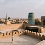 Boy standing on the ramparts of Khiva’s Kuhna Ark fortress with panoramic views over Itchan Kala’s minarets and domes.