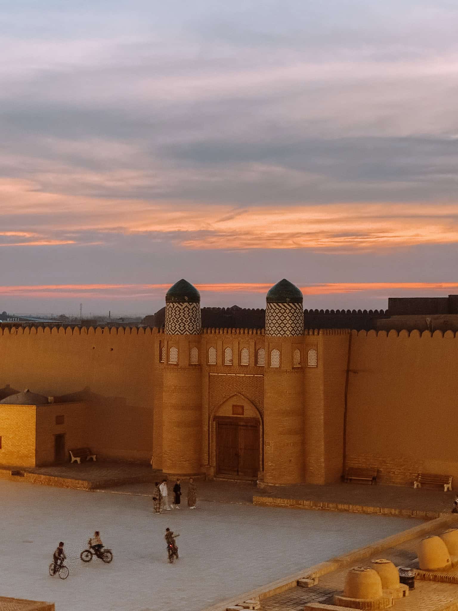 Sunset over Khiva’s Kuhna Ark fortress with locals biking through the courtyard — one of the most atmospheric moments in the city.