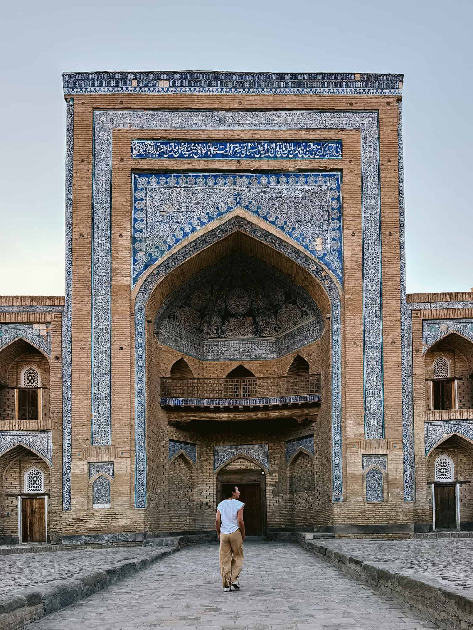 Traveler walking through the arched entrance of a blue-tiled madrassa in Khiva’s old town, surrounded by intricate Islamic design.