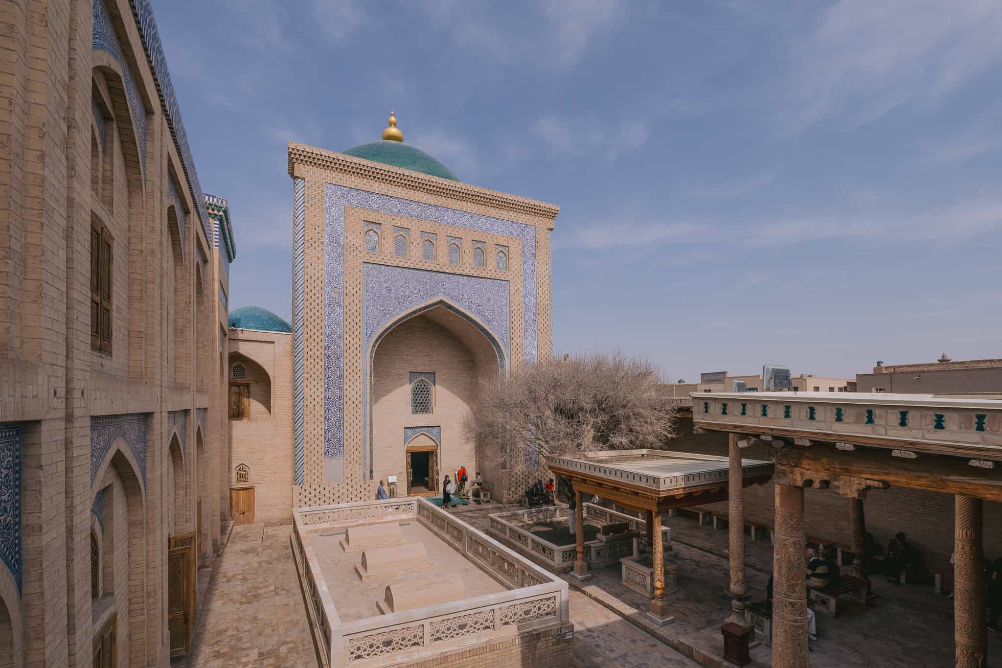 Courtyard of Pahlavon Mahmud Mausoleum in Khiva, Uzbekistan, with blue-tiled domes and carved wooden columns.