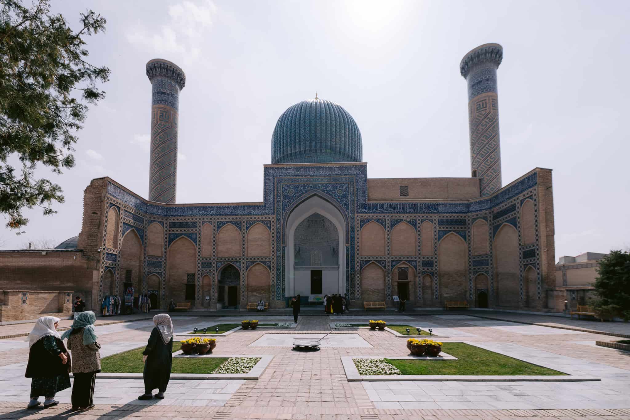 Visitors standing in front of Gur-e-Amir Mausoleum in Samarkand, Uzbekistan, with blue dome and Timurid architecture