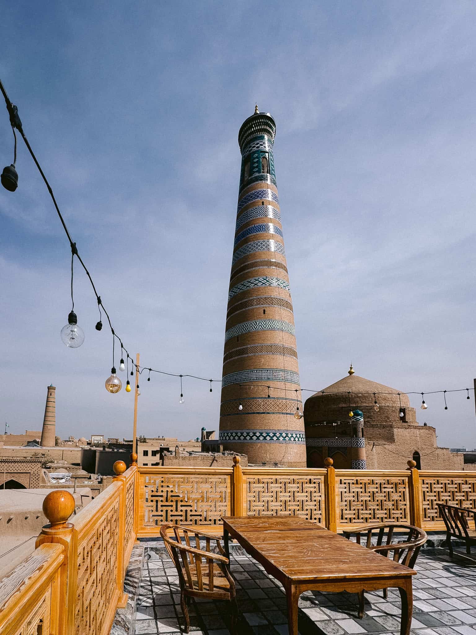 Rooftop dining view of Kalta Minor Minaret in Khiva, Uzbekistan with traditional wooden terrace seating