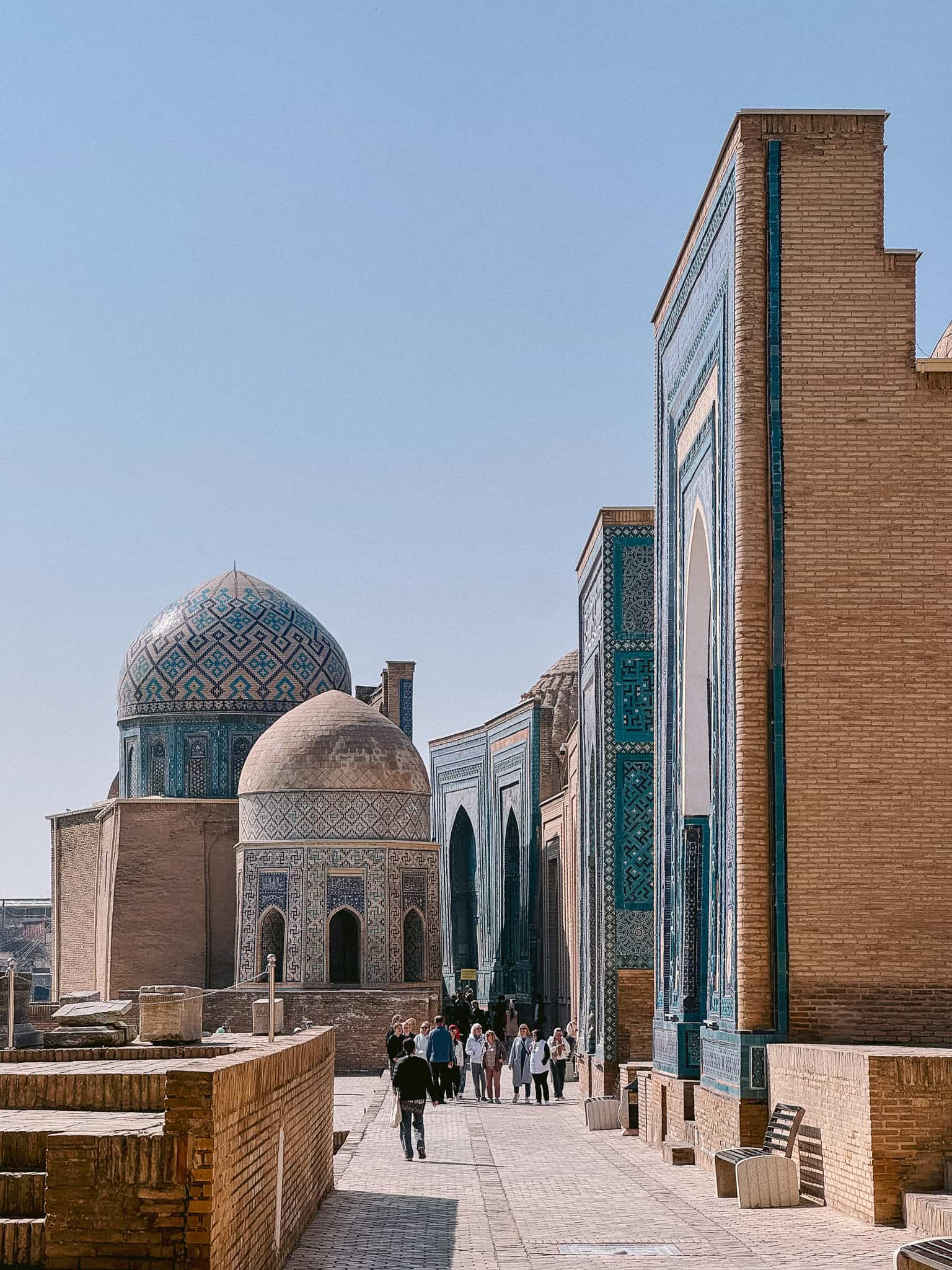 Shah-i-Zinda necropolis in Samarkand with blue-tiled mausoleums and visitors walking the pathway